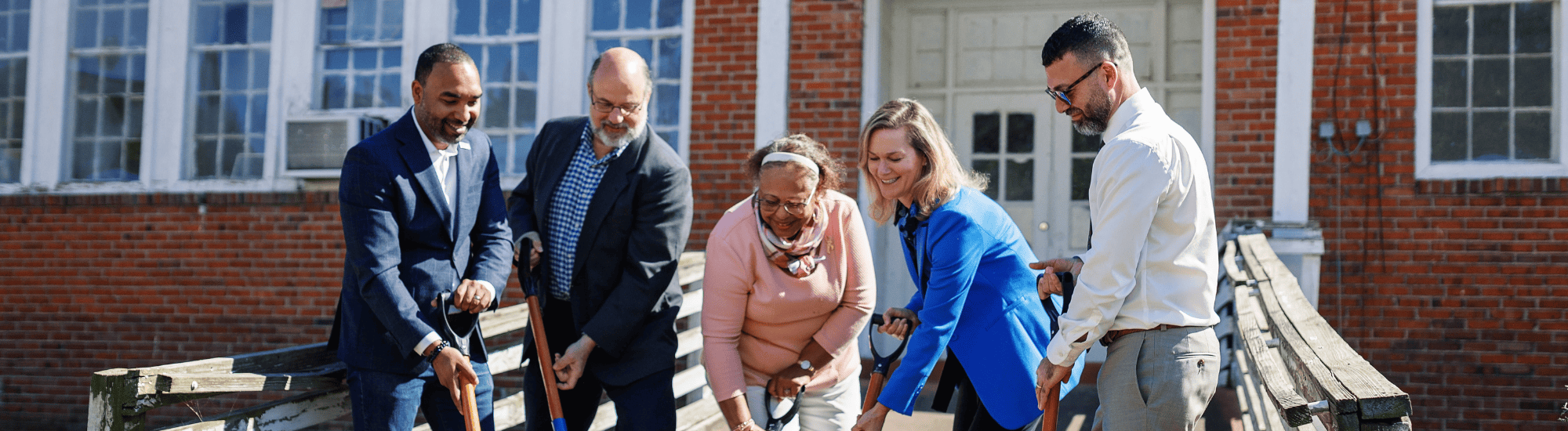Five individuals are shoveling dirt during the Ford Community Center's groundbreaking ceremony.
