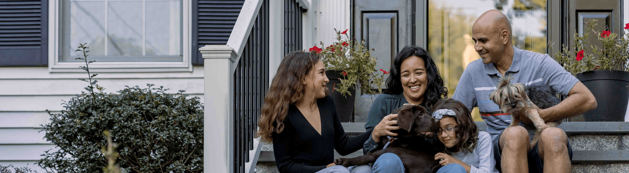 A happy family is sitting on the front steps of their house with their dog..