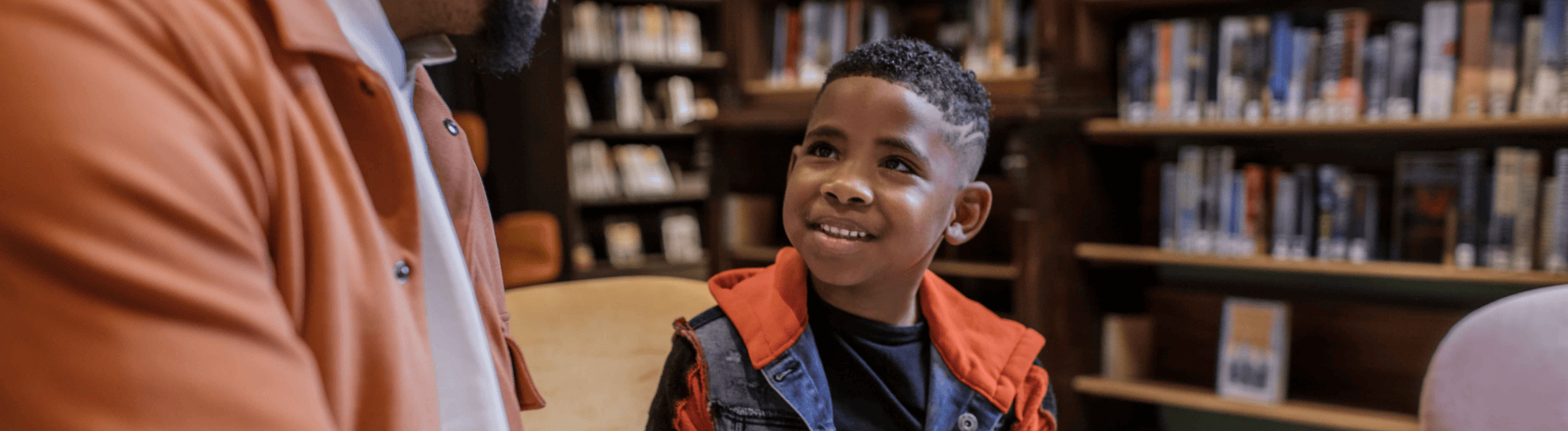 A boy is listening to a man read. him a book in the library.