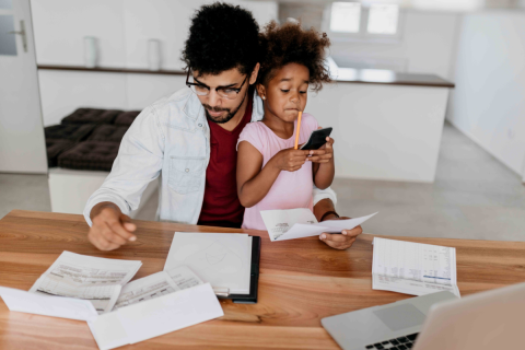 A father is holding his daughter on his lap while looks at important documents on his desk.