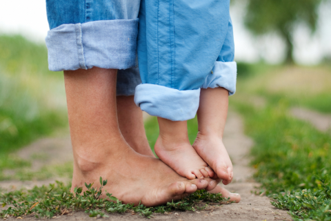 A child is standing on the feet of a caring adult.