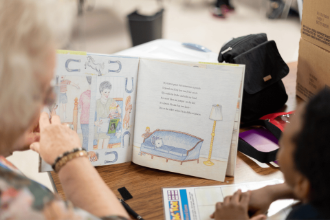 A volunteer coach is reading to a student.